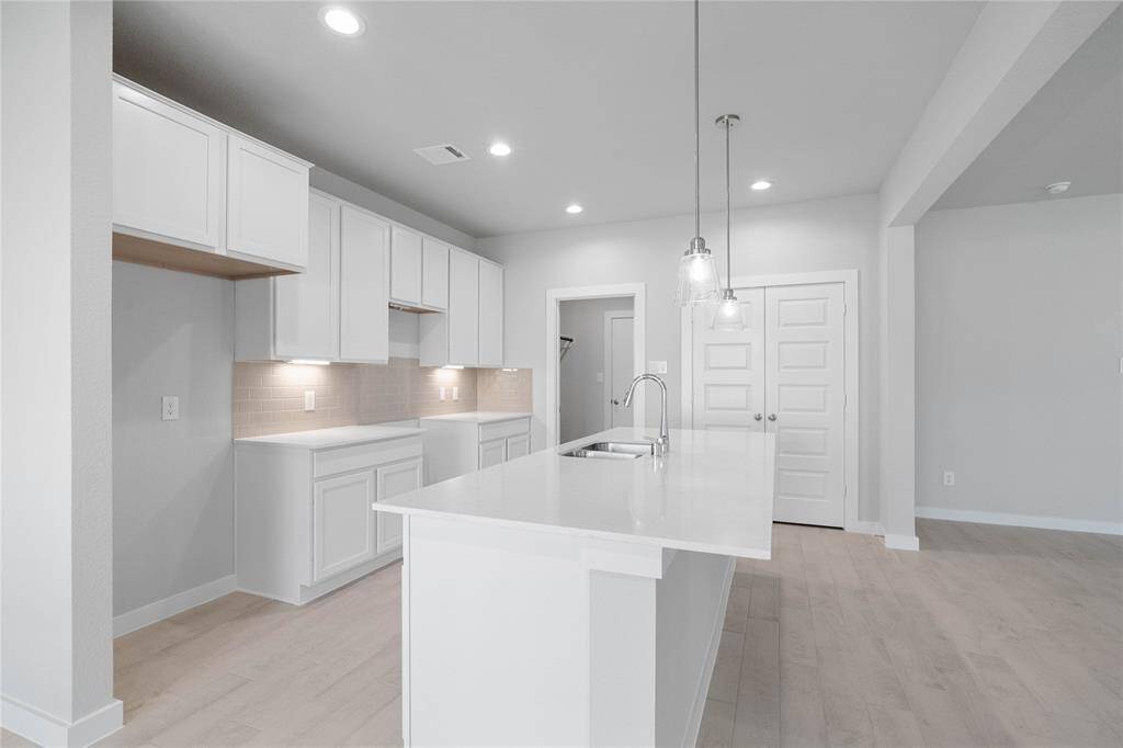Additional view of this gorgeous kitchen featuring stained cabinets, quartz countertops, kitchen island with extended countertop for breakfast bar, high ceilings with recessed and pendant lighting, and a pantry!