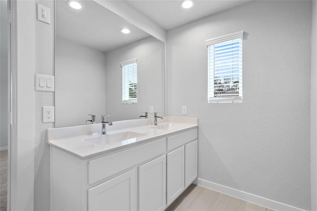 Wow! Look at this primary bathroom! Complete with stained cabinets with sleek light countertops and dual vanities, large modern tile flooring, walk in shower with tile surround, large soaking tub, and a window allowing in the natural light.