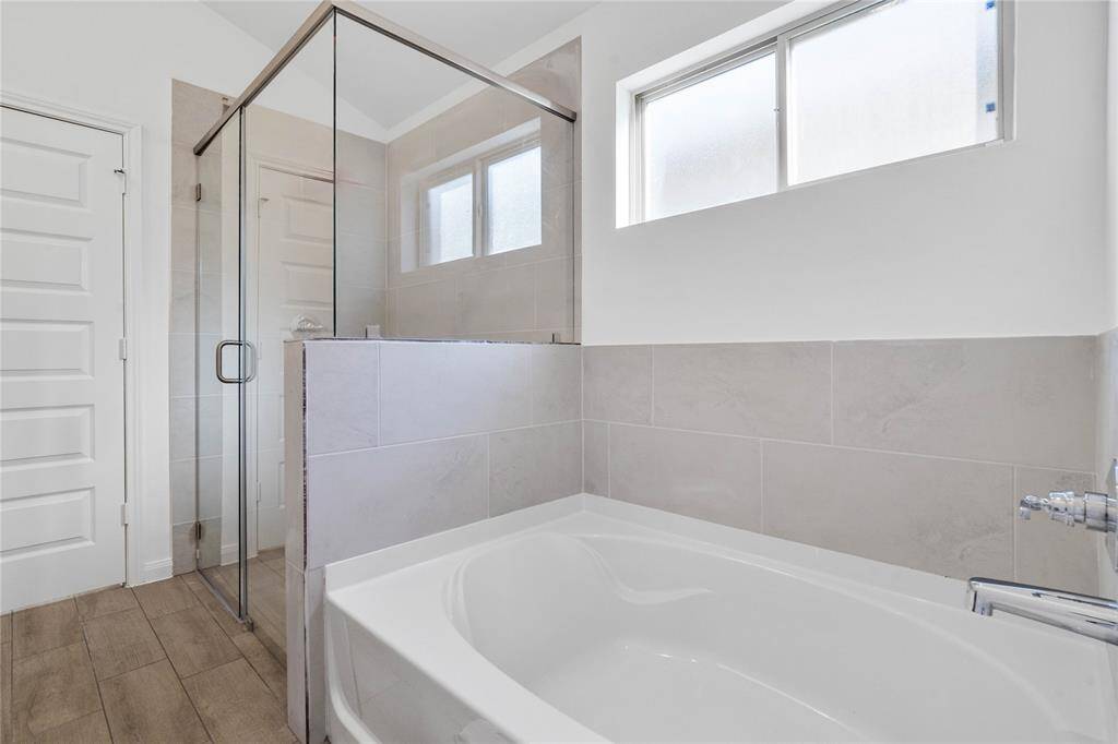Another view of the primary bathroom showcases the walk-in shower with tile surround and a separate garden tub for soaking after a long day with custom tile detailing.