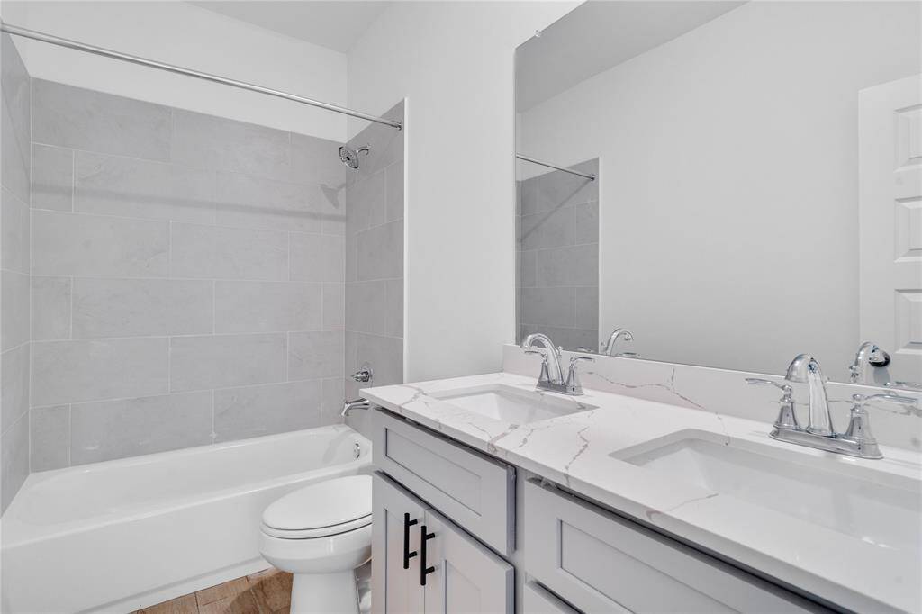 Secondary bath features tile flooring, bath/shower combo with tile surround, stained wood cabinets, beautiful light countertops, dual vanities, mirror, sleek fixtures and modern finishes.