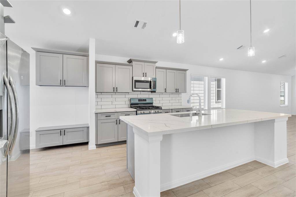 This kitchen will not disappoint! Your family and guests will enjoy many nights of fun, food and entertainment with ample counter space and kitchen island for setting up a wonderful array of provisions. This view of this gorgeous kitchen showcases SS appliances, silestone countertops, beautiful tile backsplash, gas range, double oven, high ceiling, recessed and pendant lighting and tile floors!