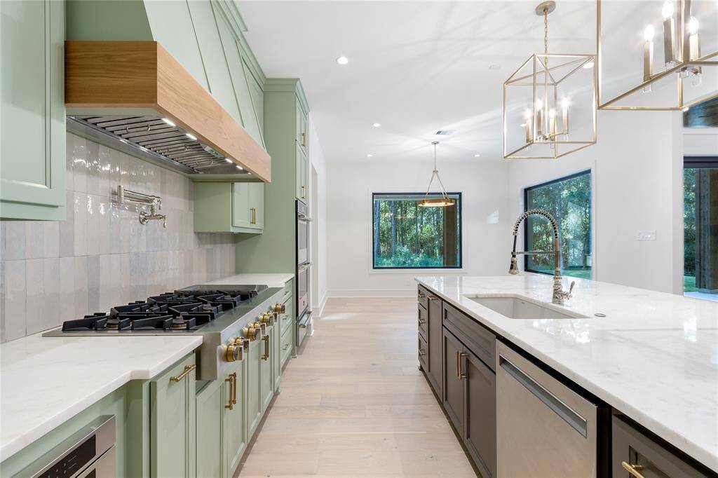 The kitchen is well-lit with natural light from a large window and stylish pendant lighting, set against a backdrop of neutral walls and light hardwood flooring. Convenient pot filler for the chef in the family!