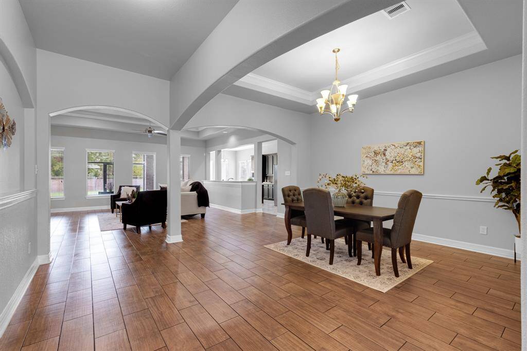 This is a spacious, open-concept living and dining space with high ceilings, elegant archways, and ample natural light. The area features hardwood flooring and a contemporary chandelier, providing a modern yet inviting atmosphere.