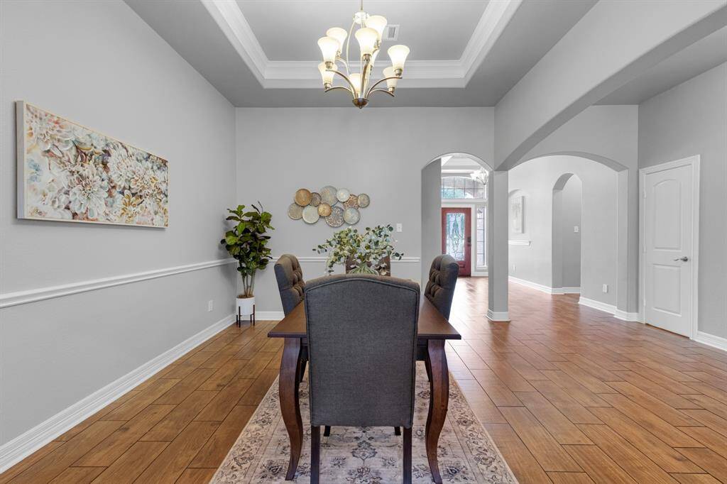 This is an elegant dining space featuring hardwood floors, a tray ceiling with a chandelier, and tasteful wall art. The room is framed by archways leading to other parts of the home, creating an open and inviting atmosphere.