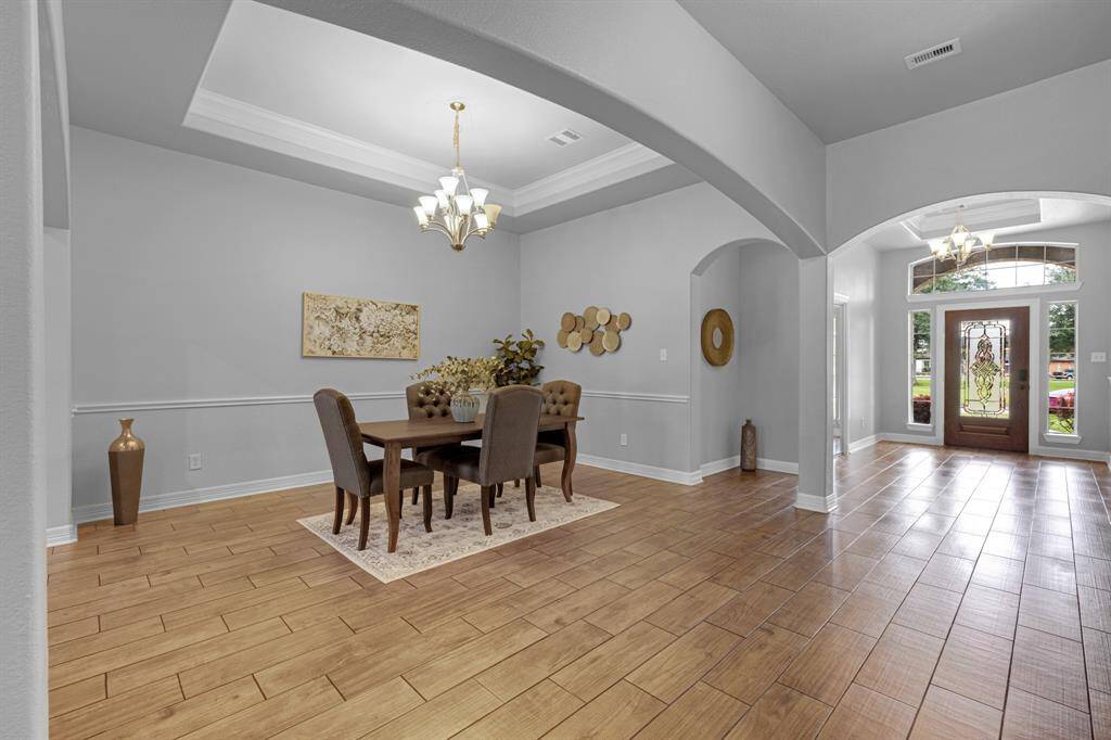 Spacious dining area with elegant tray ceiling, hardwood floors, and ample natural light from the large front window.