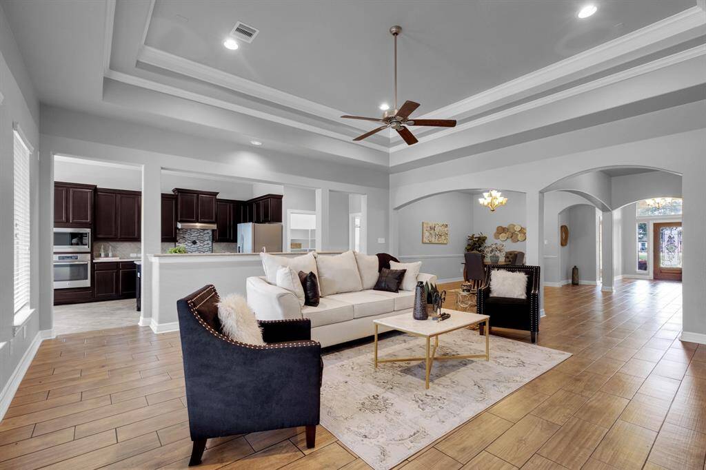 This photo showcases a spacious open-concept living area with elegant coffered ceilings and hardwood floors. It seamlessly connects to a modern kitchen with dark wood cabinetry and stainless steel appliances. The room is filled with natural light and features tasteful, contemporary decor.