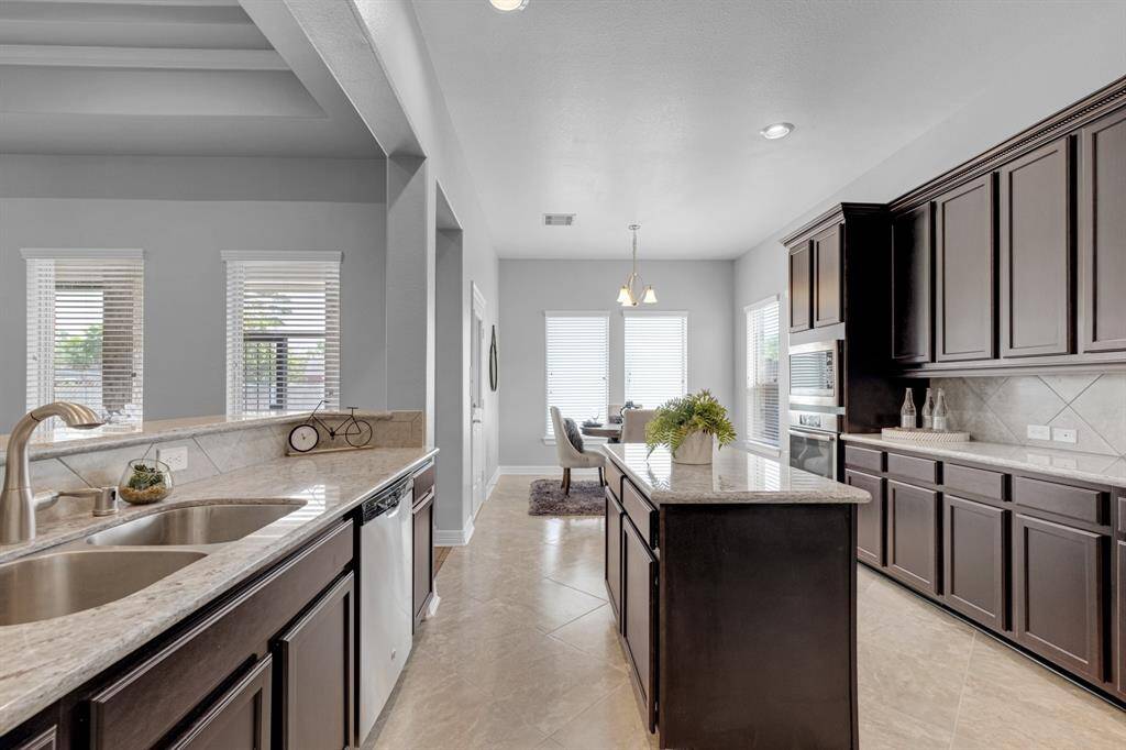 Modern kitchen with sleek dark cabinetry, granite countertops, stainless steel appliances, and a central island. Features ample natural light and an open-plan layout leading to the living area.