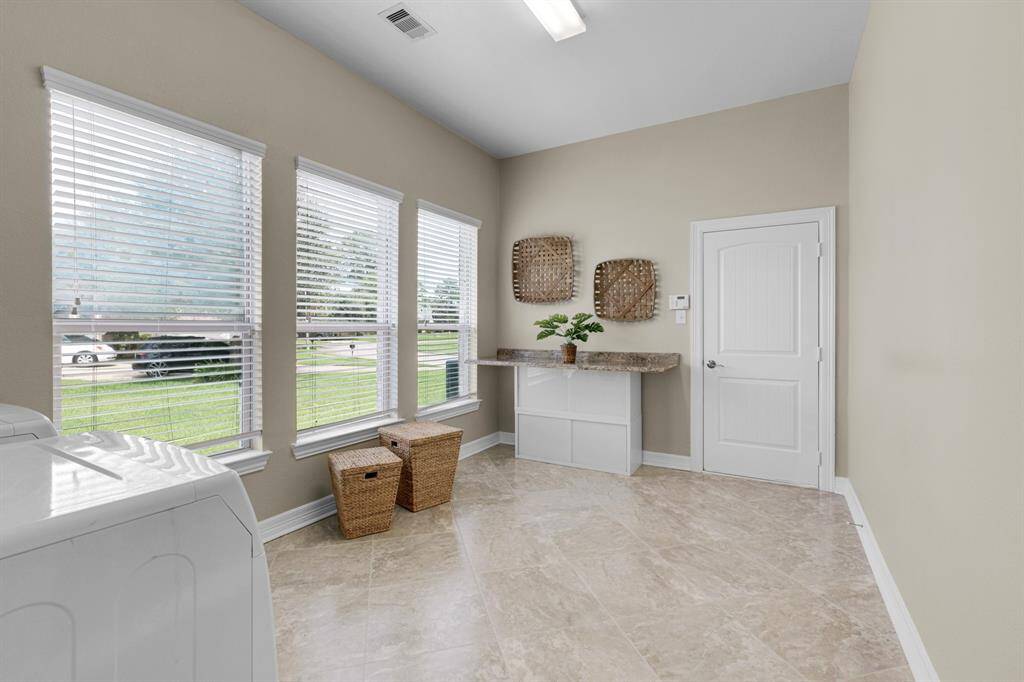 This is a bright, airy room featuring large windows with blinds, neutral wall colors, and tile flooring. It includes a built-in cabinet with a countertop and space for storage baskets.