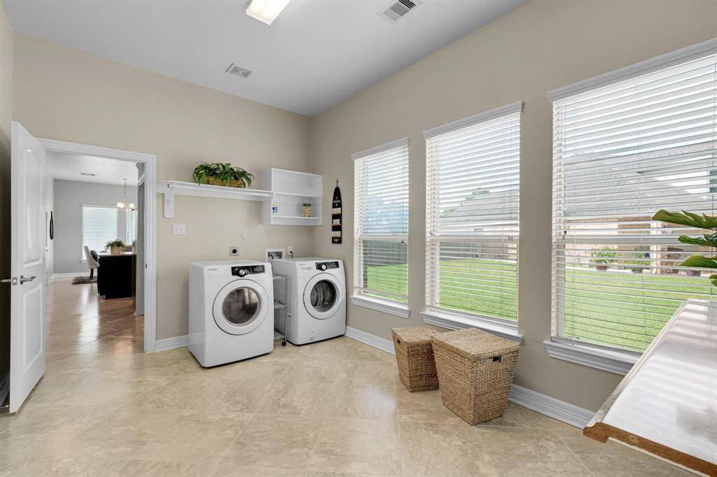 This is a bright and spacious laundry room featuring modern appliances, abundant natural light from large windows, and easy access to other parts of the home.