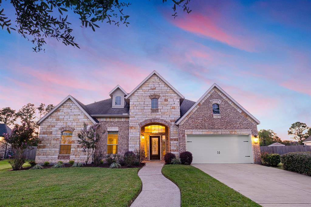 This is a single-family home featuring a brick facade with an arched entrance, a two-car garage, and a well-manicured lawn, captured during a beautiful sunset.