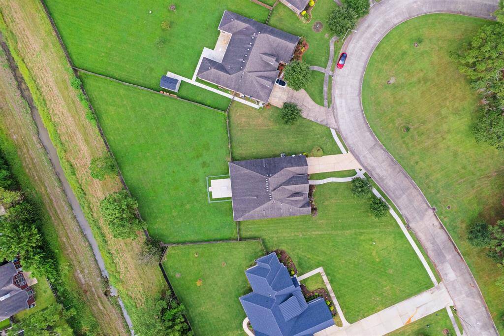 This aerial photo showcases a large, detached house with a spacious, well-maintained lawn, situated in a quiet cul-de-sac with an adjacent green open space and a small watercourse running along one side of the property.