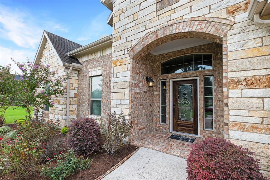 Charming home entrance featuring a decorative glass door framed by an elegant stone archway, complemented by a well-manicured garden with colorful foliage.