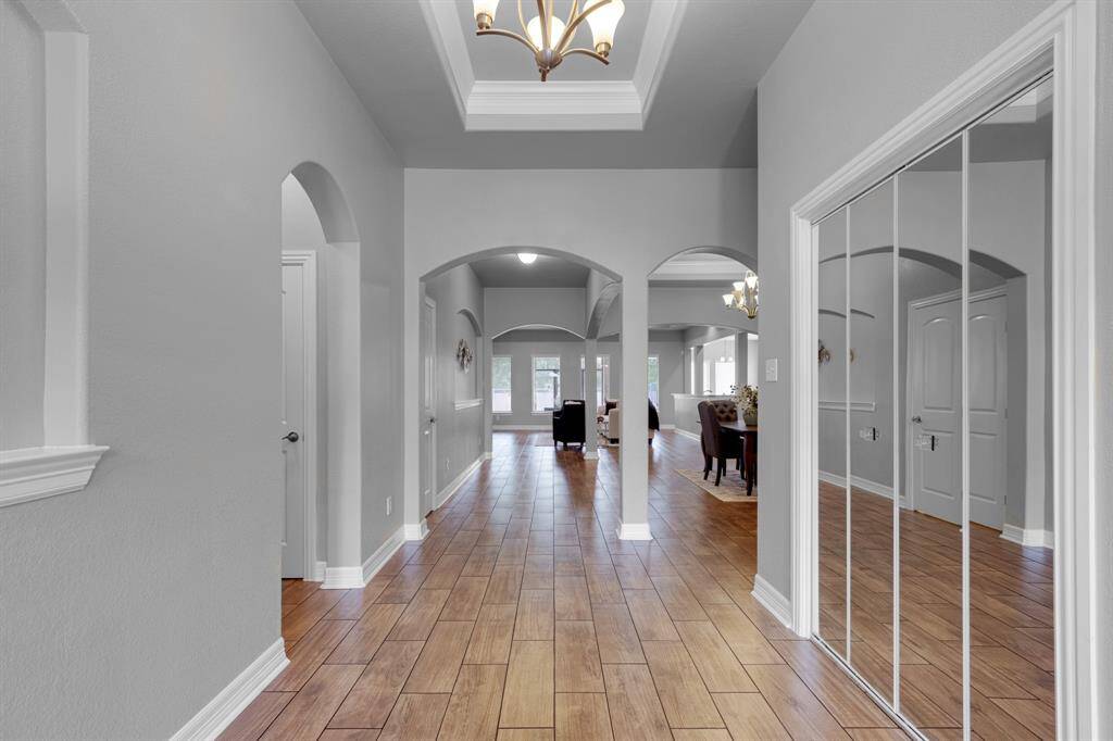 This is a spacious hallway with elegant archways, hardwood floors, and a raised ceiling with a classic chandelier, leading into a formal dining area. The area is well-lit and features neutral colors, providing a versatile backdrop for various decorating styles.