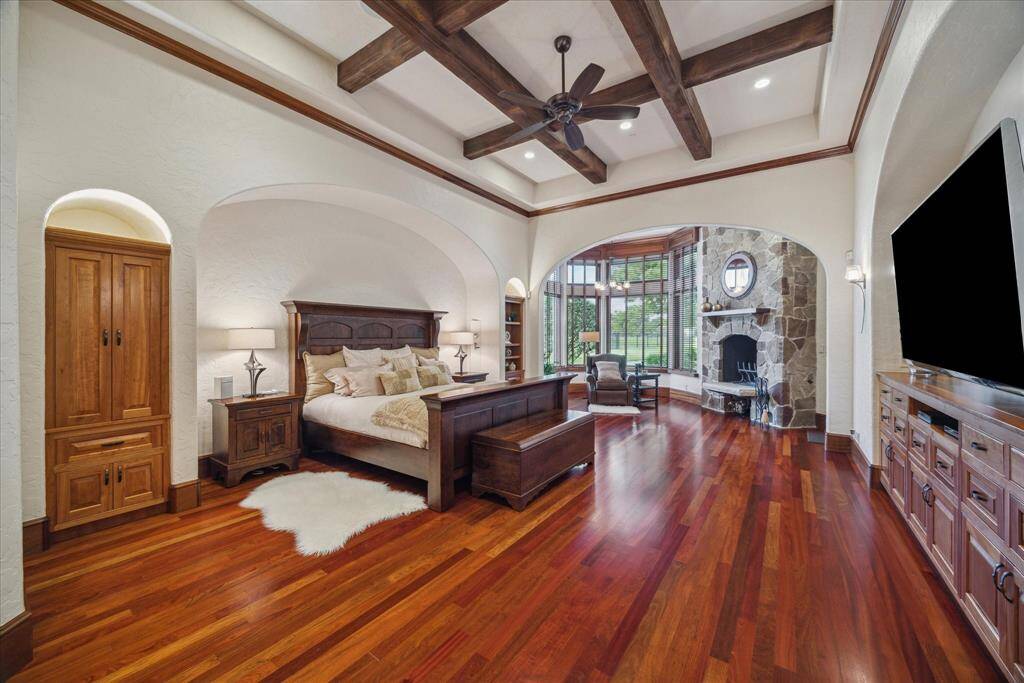 Tucked away from the public spaces behind arched double doors is an enormous primary bedroom sanctuary. An arched recess forms the ideal location for the bed and creates an intimate, cozy feel in this large space accented by intersecting wood beams on the tray ceiling. Morning coffee is accessible bedside as there is a built-in dry bar and mini fridge for cooling creamer or bottled water! A discreet built-in electronic safe is bedside for easy and secure access at a moment’s notice.