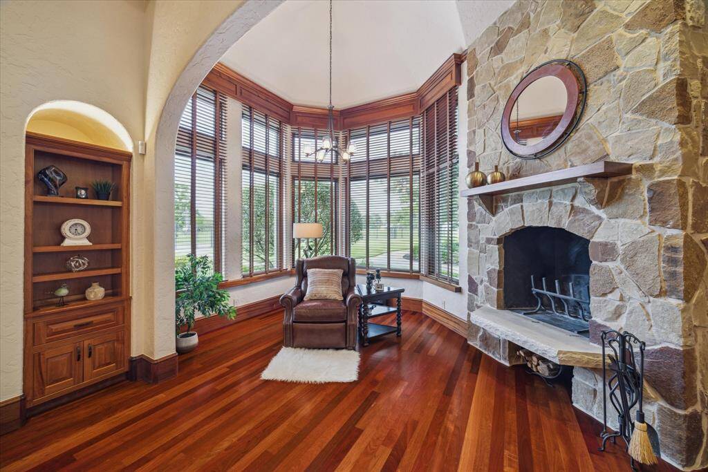 The sitting area within the primary bedroom suite features a stone wood burning fireplace with chiseled natural stone hearth and walls of floor to ceiling windows, naturally creating a private sanctuary. A French door provides a direct escape to the backyard oasis, perfect for a quiet dip in the pool.