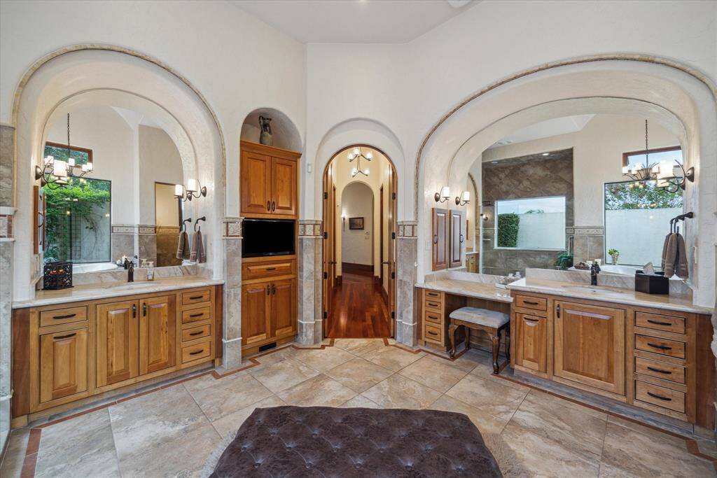 The en-suite primary bathroom is an oasis of calm, providing relaxation for the body, mind and spirit. It features dual vanities nestled beneath architectural arches delicately trimmed in mosaic tile as well as a dedicated makeup vanity topped with natural stone countertops and accompanying built in medicine cabinet with electrical outlets to discreetly contain appliances such as hair dryers.