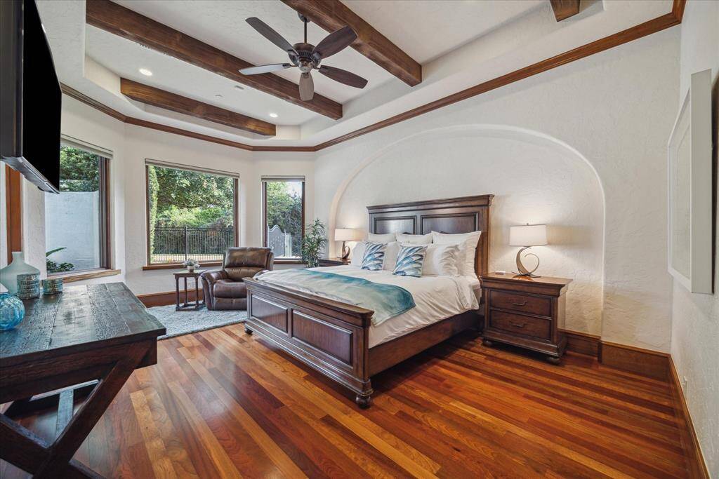 The third guest suite functions as an additional primary bedroom suite. It is generously sized, boasts a tray ceiling with beams, art niche, hardwood floors, three oversized windows with motorized Lutron shades, 8” baseboards and a larger walk-in closet with custom built-ins.