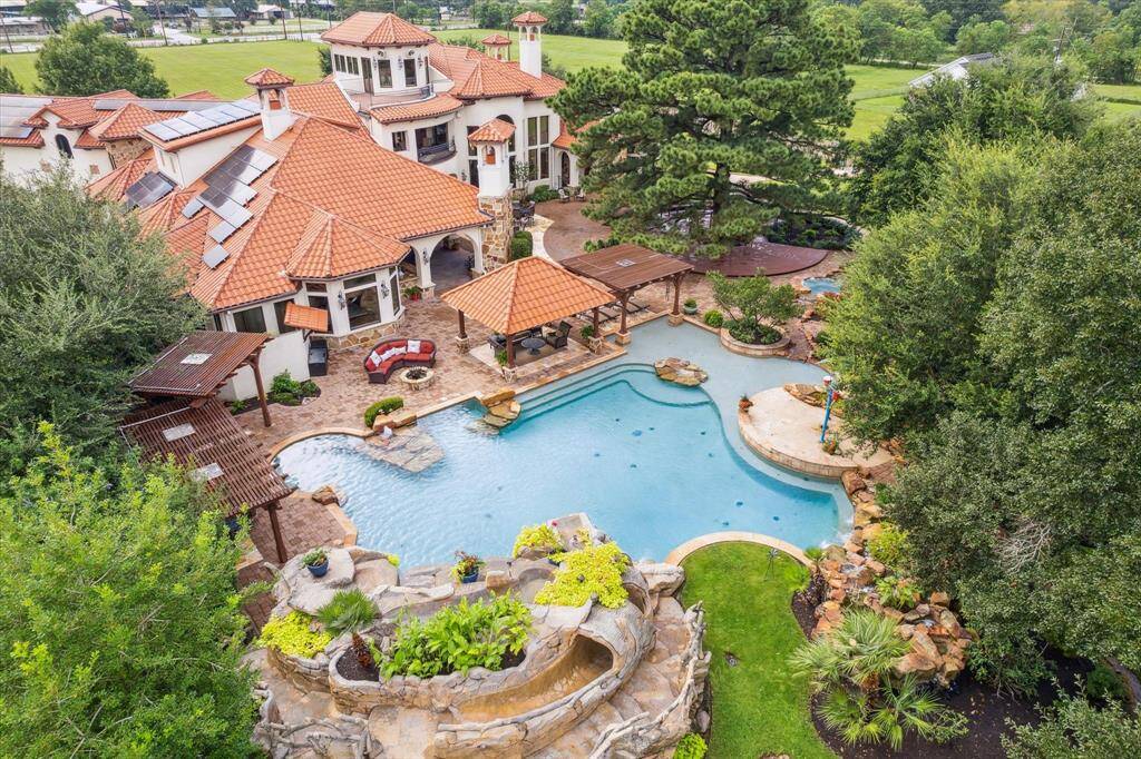 An aerial view of the pool and patio area resembles a resort. This pool oasis is a serene backdrop for entertaining. The pool is sport depth for kids of all ages and facilitates water sports. The home’s waterpark includes a pool, a hot tub linked to the main pool by gently overflowing into the stream, a waterslide, waterfall, grotto and splash pad!