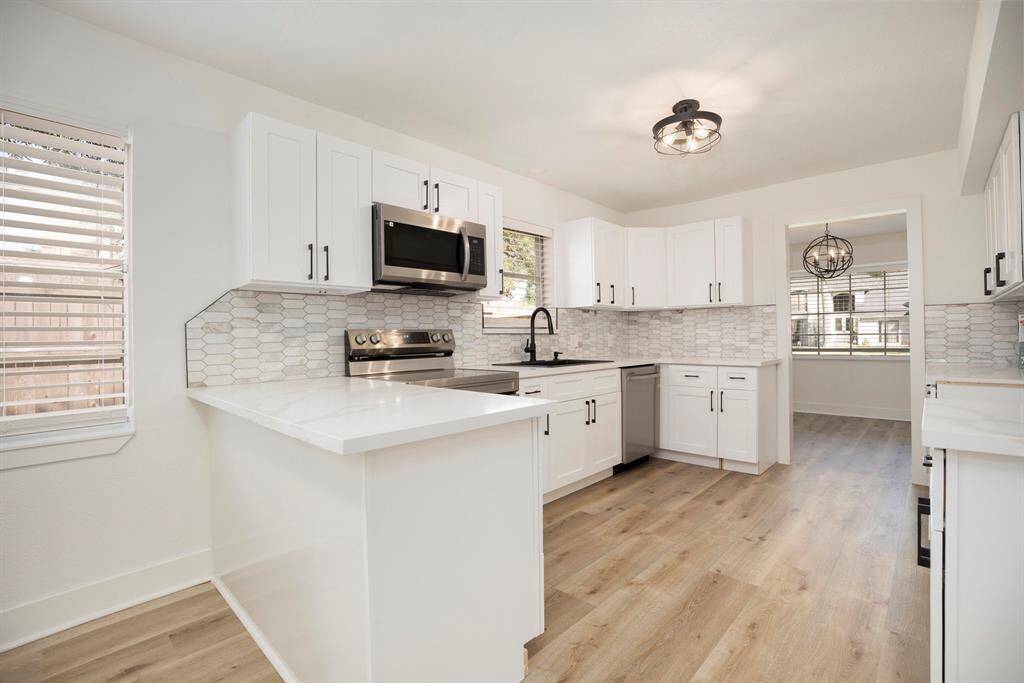 This is a bright, modern kitchen featuring white cabinetry, stainless steel appliances, a subway tile backsplash, and wood-look flooring. It has ample storage and prep space making it ideal for cooking and entertaining.
