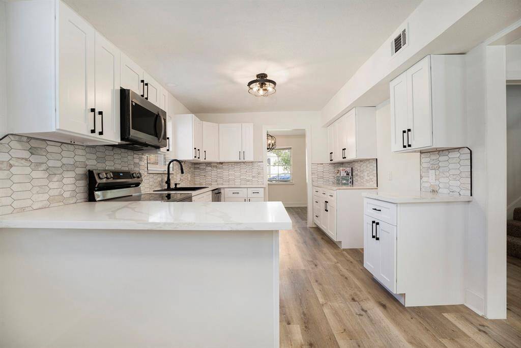 This is a modern kitchen with white cabinetry, stainless steel appliances, and a hexagonal tile backsplash.