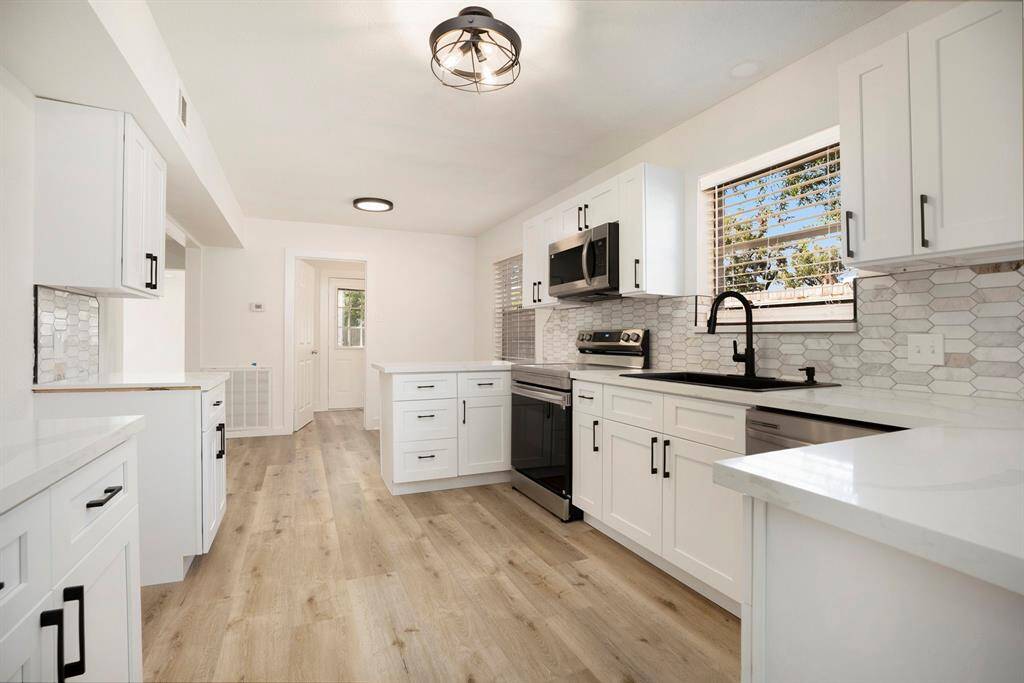 This photo features a modern, bright kitchen with white cabinetry, stainless steel appliances, sleek countertops, and a stylish backsplash. The space is complemented by natural light and neutral flooring.