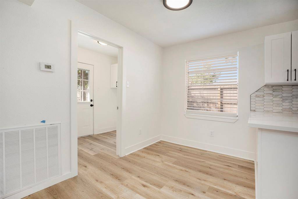 This is a bright, modern breakfast area with fresh white walls, neutral flooring, and a large window allowing for natural light. There's also a built-in shelving unit next to a doorway leading to the laundry room.