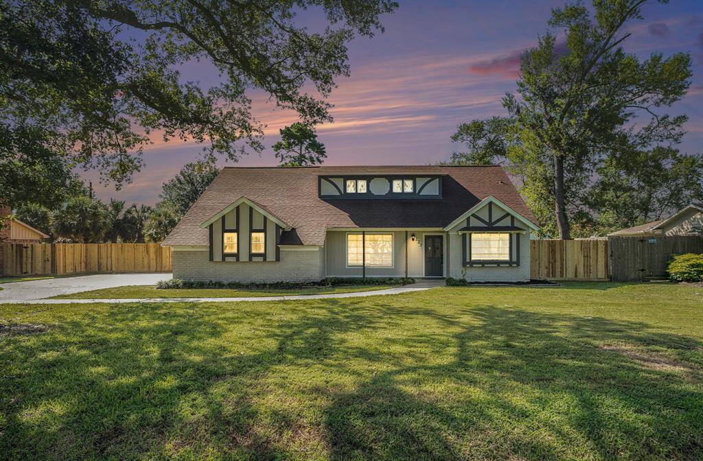 Charming home with a Tudor-style facade, featuring a spacious driveway, large windows, and a backdrop of a beautiful sunset sky. The property includes a well-maintained lawn and privacy fencing.