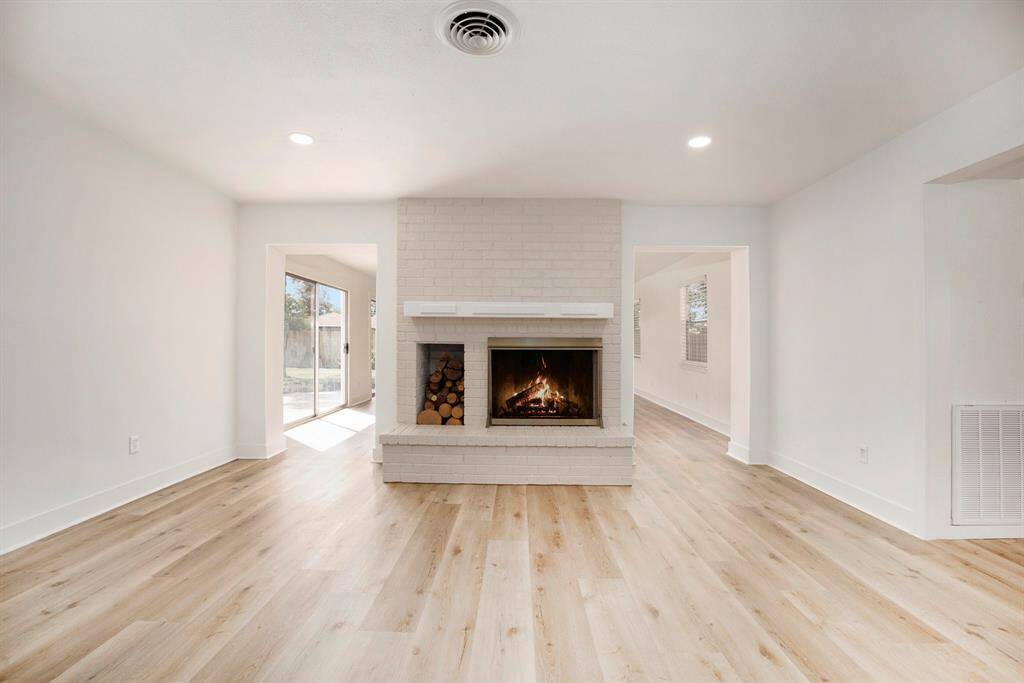 This is a bright, spacious living area with a cozy fireplace and modern flooring. Large windows provide ample natural light, and the room features clean, white walls and recessed lighting.