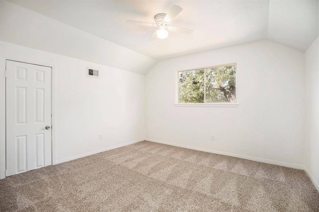 This is a bright, empty room with fresh neutral paint, a carpeted floor, a ceiling fan, and a window offering a view of greenery.