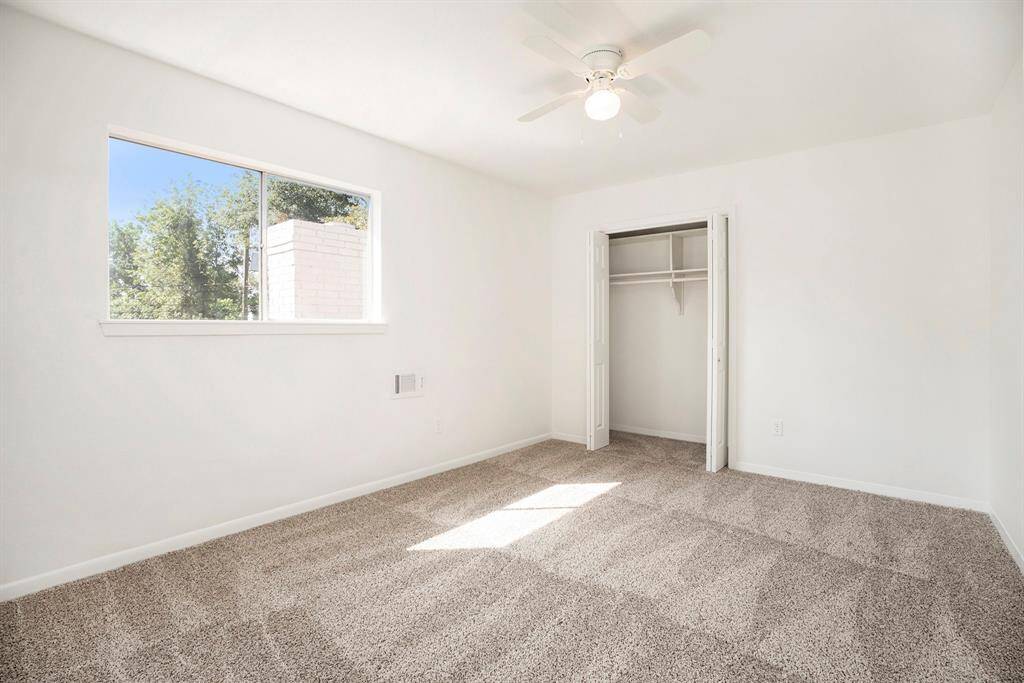 This is a bright secondary upstairs bedroom featuring plush carpeting, a large window that allows for plenty of natural light, and a ceiling fan for additional comfort. The room also includes a built-in closet for storage.