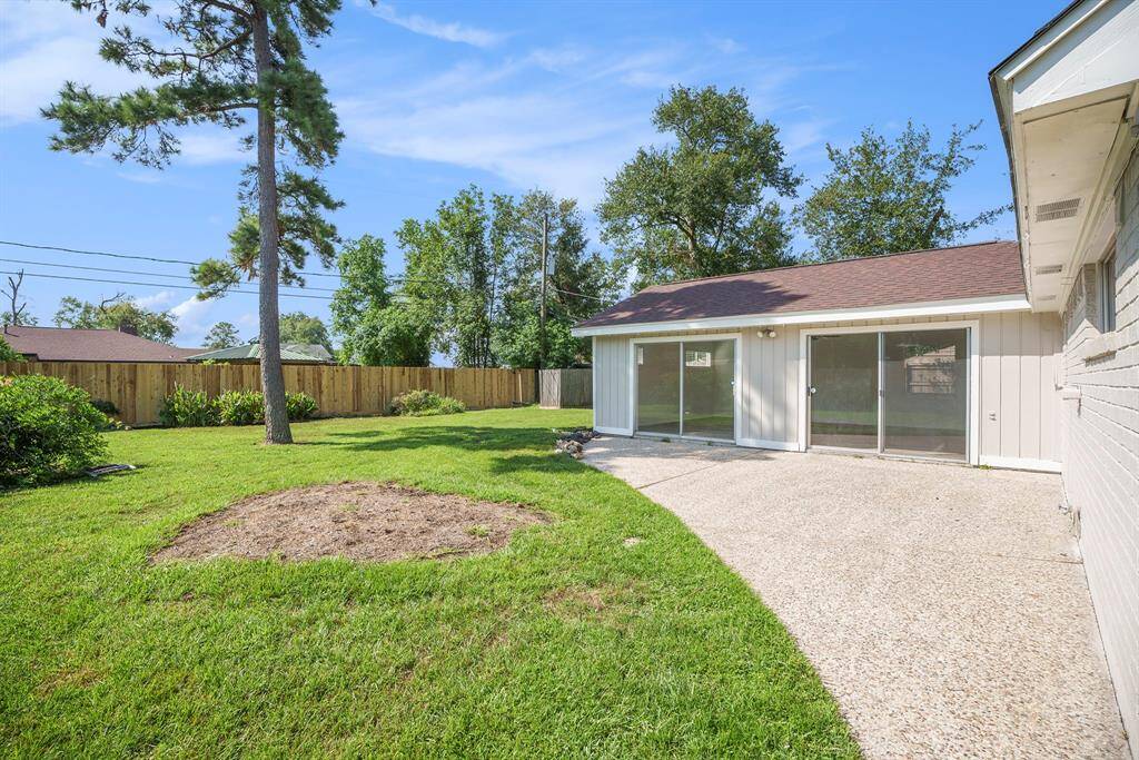 This is a spacious backyard with a well-maintained lawn, a mature tree providing shade, and a privacy fence. The home features two sets of glass sliding door leading to a concrete patio area, ideal for outdoor living and entertaining.