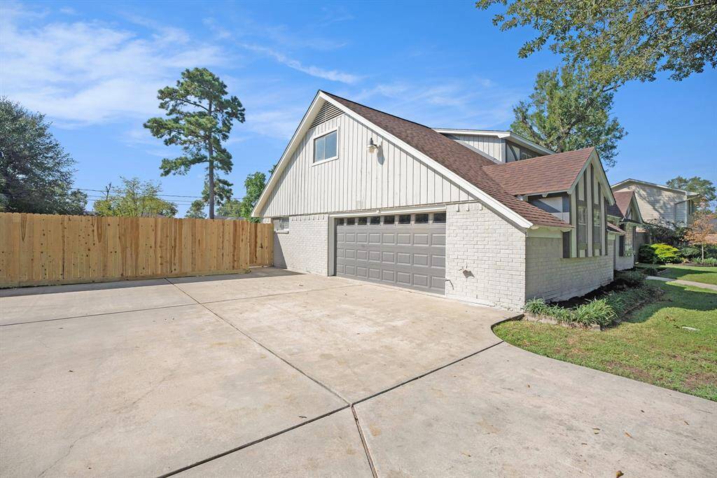 This is a two-story home with a fresh painted exterior, featuring a large driveway and an attached two-car garage. The property includes a new wooden privacy fence and is surrounded by mature trees, offering both space and seclusion.