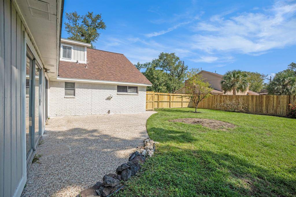 This is a spacious backyard with well-maintained grass, new privacy fence, and a small patio area, complementing a two-story brick home with ample natural light.