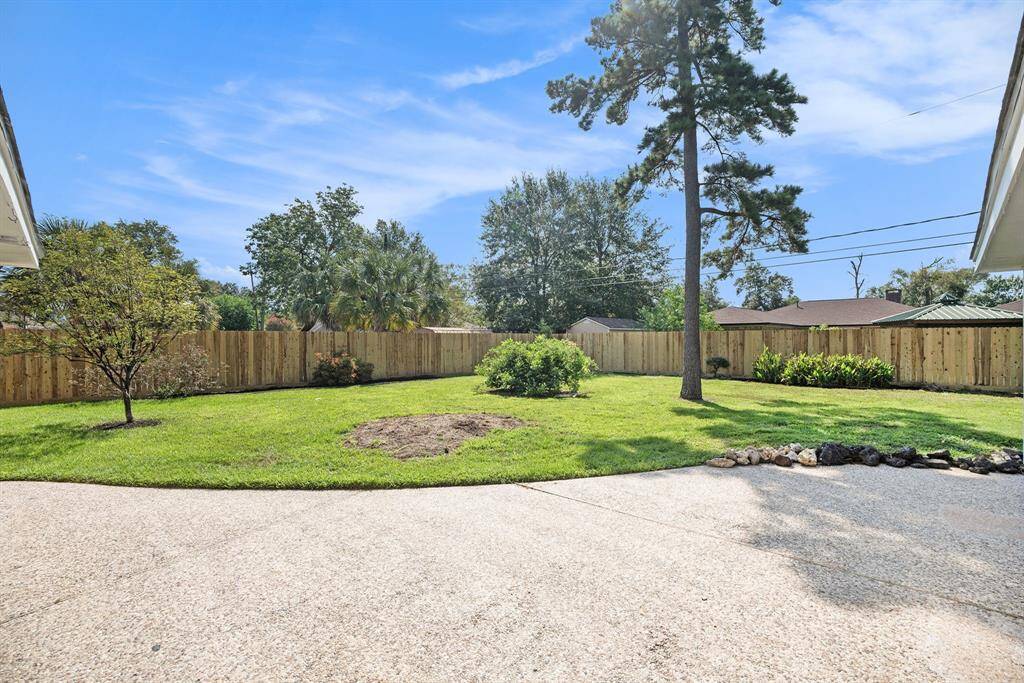 Spacious backyard with well-maintained lawn, mature trees, landscaping, and a privacy fence.