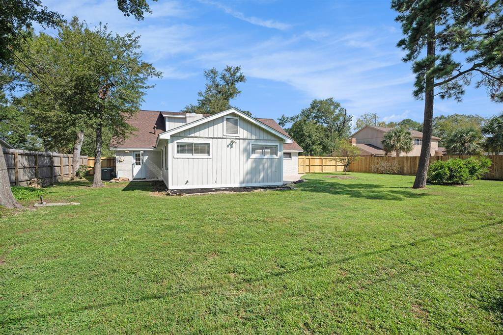You're looking at a spacious backyard with a well-maintained lawn, mature trees, and a view of the rear of a two-story home featuring an attached garage and privacy fencing, offering ample outdoor space for recreation and entertaining.