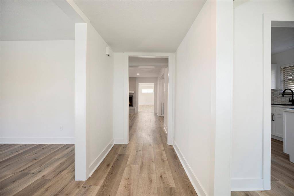 This image shows a modern, bright hallway leading towards a kitchen area, featuring clean lines and neutral colors.