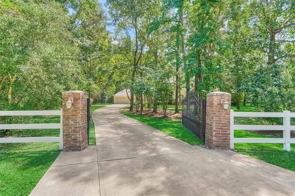 Brick pillars, an iron driveway gate, and front white vinyl fencing elevate the property entrance