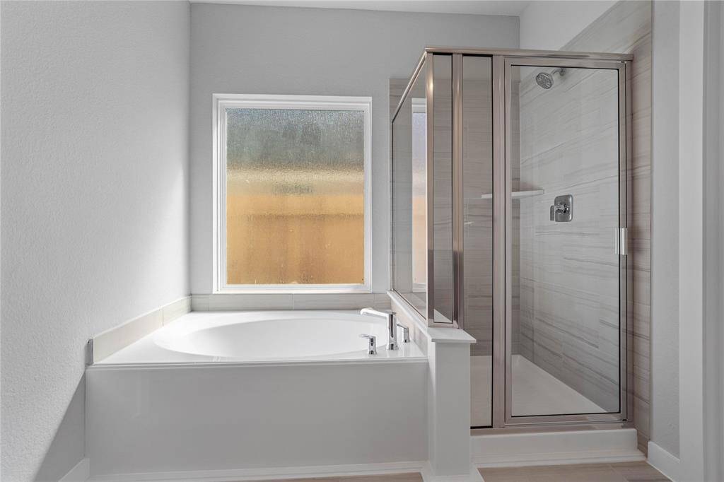 Additional view of the primary bathroom featuring the walk-in shower with tile surround and separate garden tub for soaking after a long day with custom tile detailing.