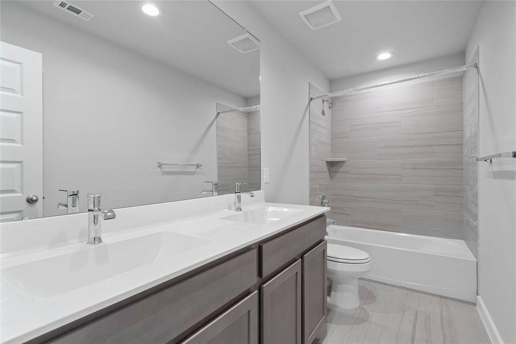 Secondary bath features tile flooring, bath/shower combo with tile surround, stained cabinets, beautiful light countertops with dual vanities, mirror, sleek fixtures and modern finishes.