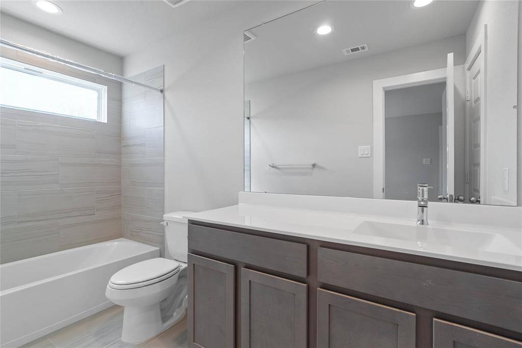Secondary bath features tile flooring, bath/shower combo with tile surround, stained cabinets, beautiful light countertops, mirror, sleek fixtures and modern finishes.