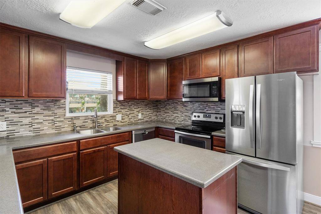 This gorgeous island kitchen was remodeled in 2018 with modern shaker style cabinets, Corian counters, stainless appliances and flooring. The refrigerator stays with the home