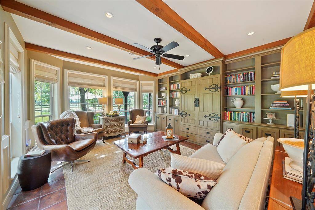 Family room features a wall of built-ins, a wood beamed ceiling, wainscoting & French doors leading to the pool.