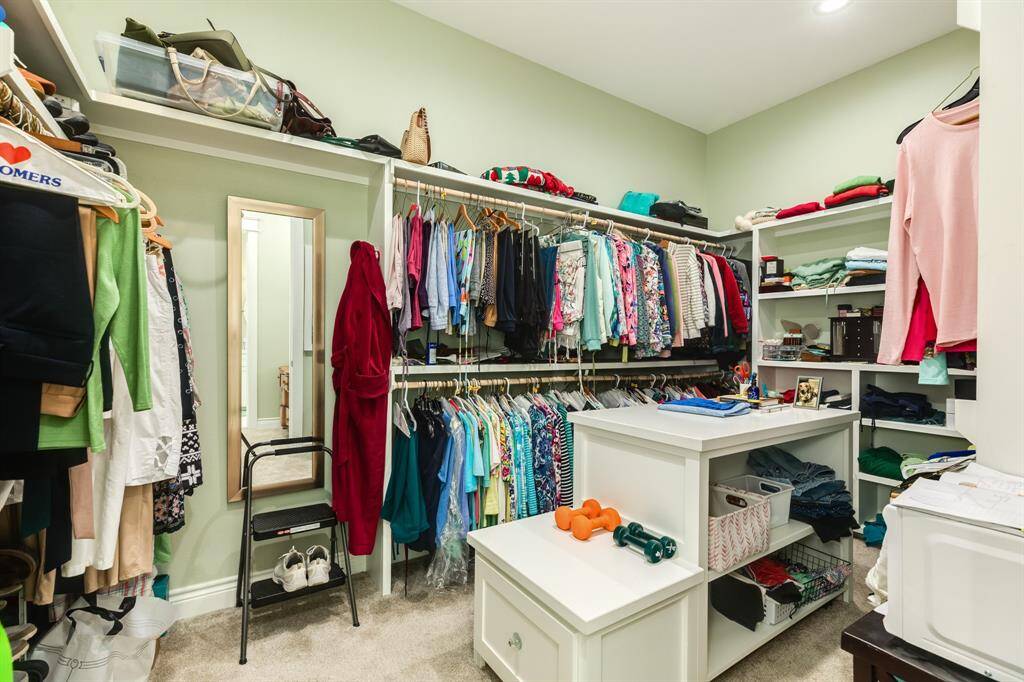Spacious walk-in closet with ample shelving, multiple hanging areas, and a built-in central storage unit with drawers. It also features overhead storage and a full-length mirror.