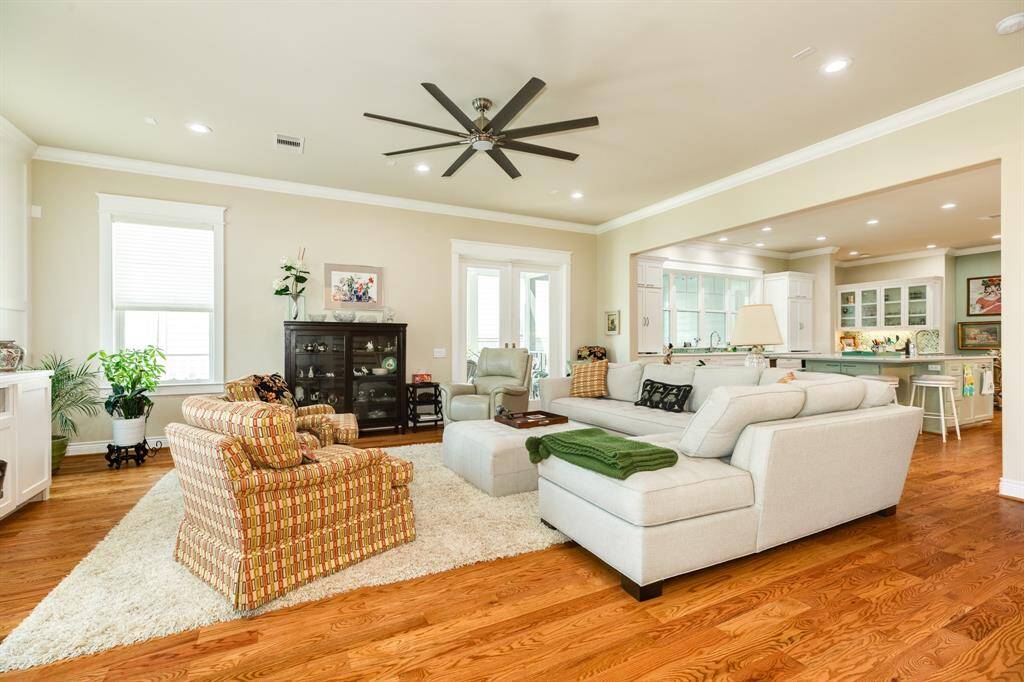 Spacious, well-lit living room featuring hardwood floors, neutral wall colors and an open-concept layout that leads to a kitchen area.