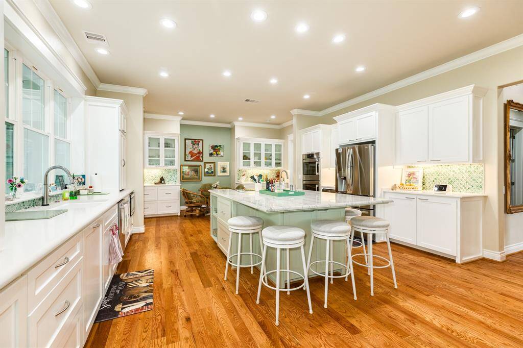 A spacious, modern kitchen featuring white cabinetry, hardwood floors, a central island with seating, and ample natural light from large windows.