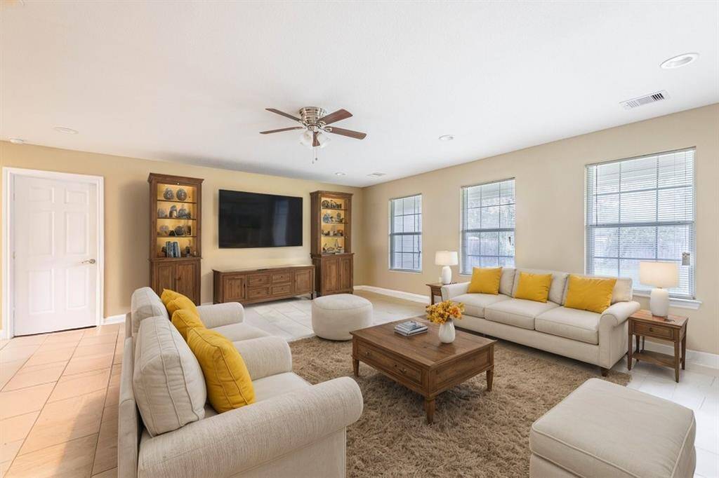 *Virtually Staged*This is a spacious, well-lit living room with neutral walls, featuring large windows, a ceiling fan, and tile flooring.