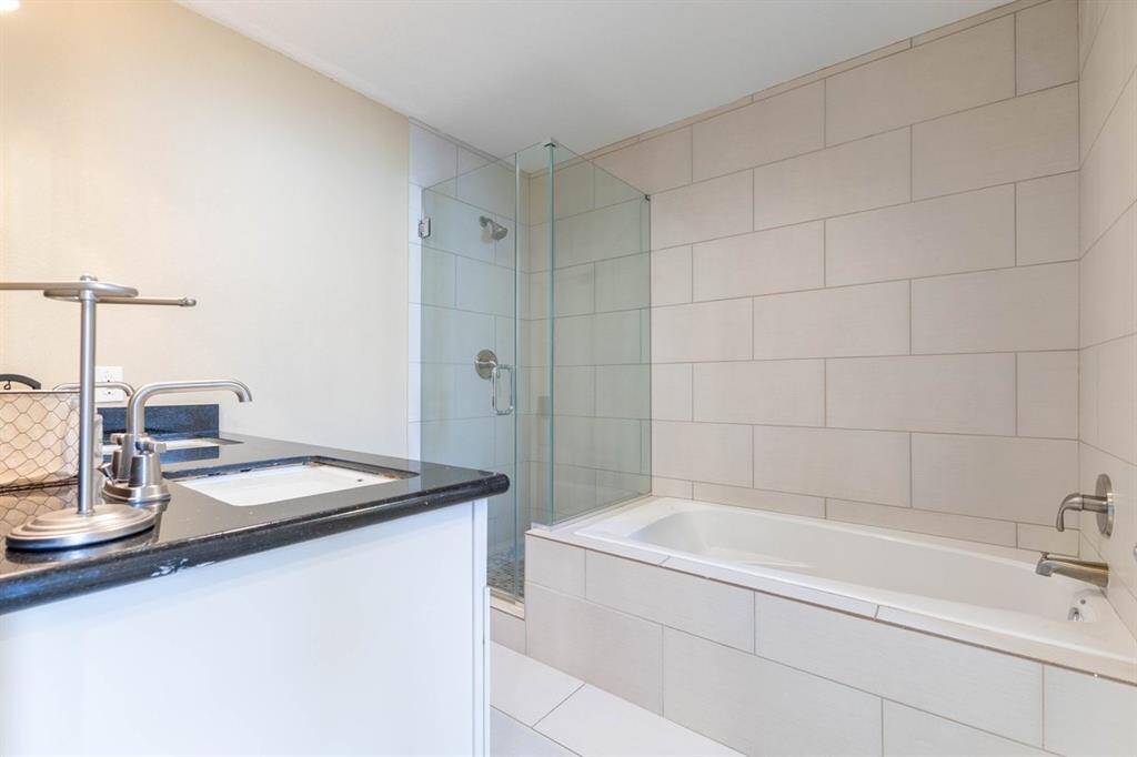 This is a modern, clean bathroom featuring a large bathtub with an overhead shower and glass doors, a single sink vanity with ample counter space, and a neutral color scheme.