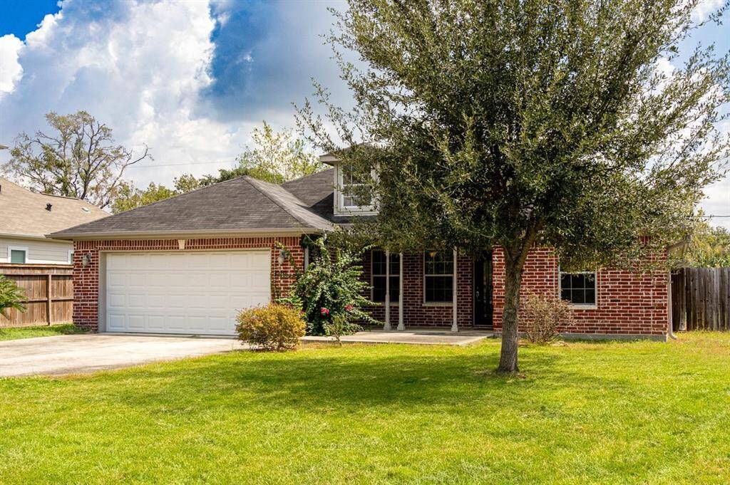This is a brick home featuring a large two-car garage, a well-maintained front lawn with a mature tree, and a welcoming entrance. The pitched roof and upper windows offer a classic suburban aesthetic.