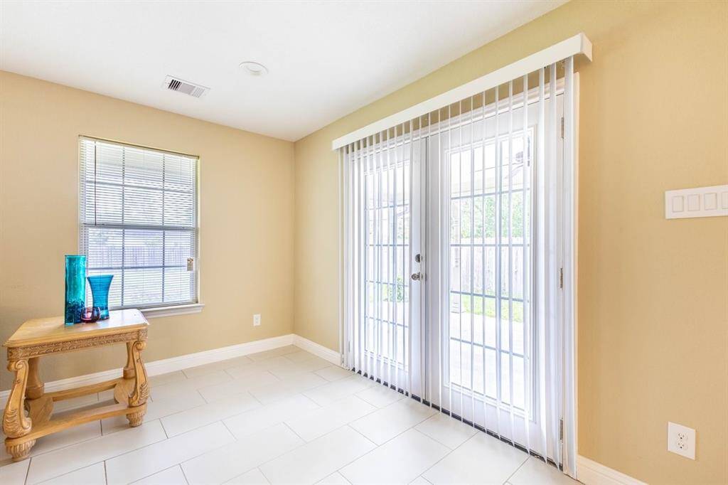 Bright and airy room with neutral walls, tile flooring, a window with blinds offering natural light, and sliding glass doors leading out, likely to a patio or backyard.