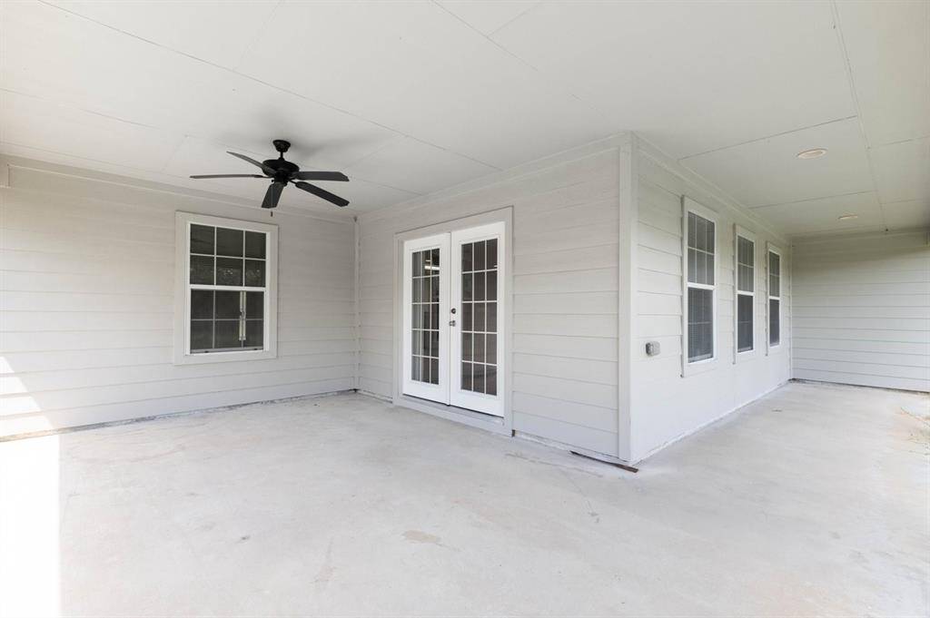 This is a spacious, covered patio area with a ceiling fan, multiple windows for natural light, and a glass-paneled door leading into the home. It offers a comfortable outdoor living space.